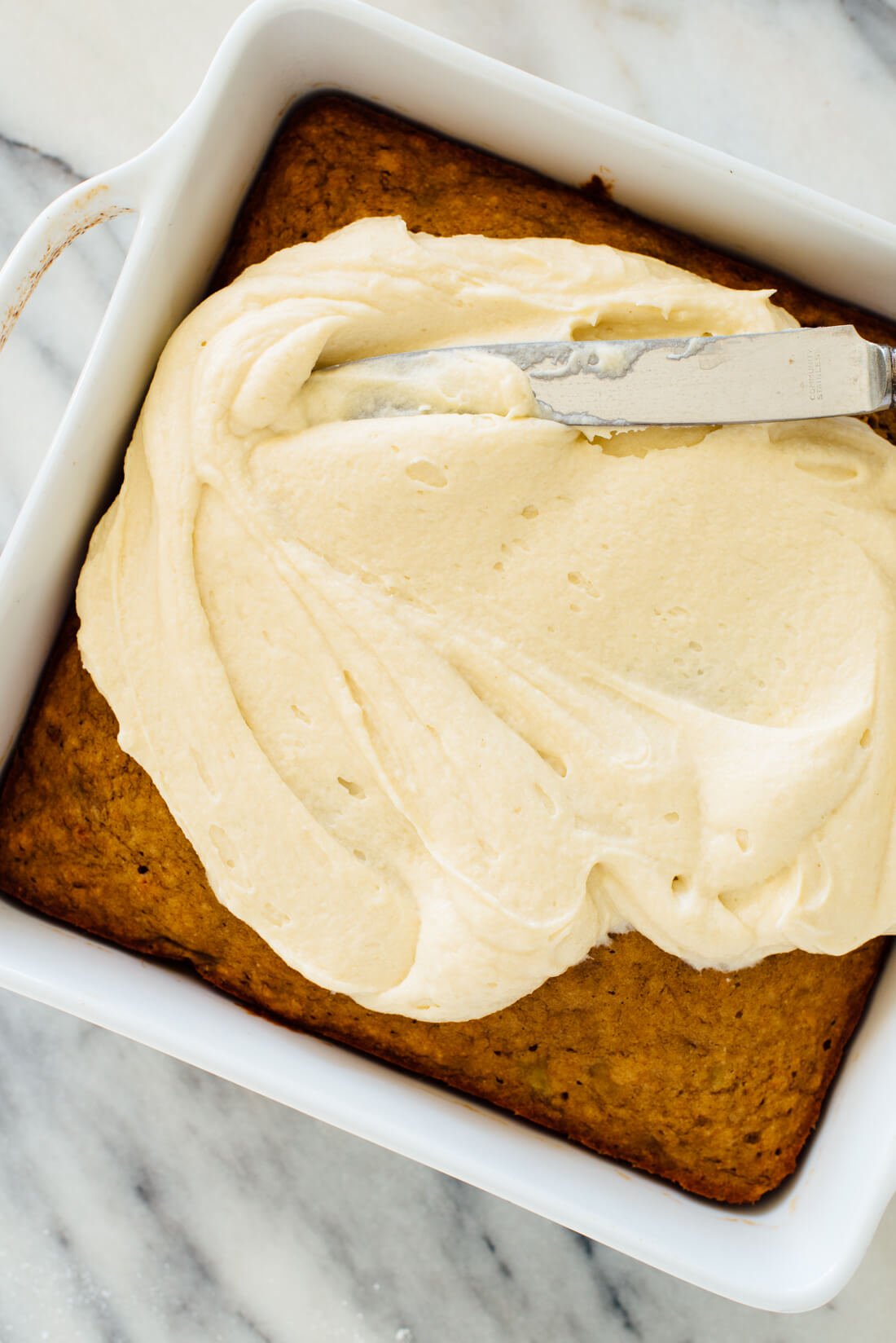 spreading cream cheese frosting on banana cake