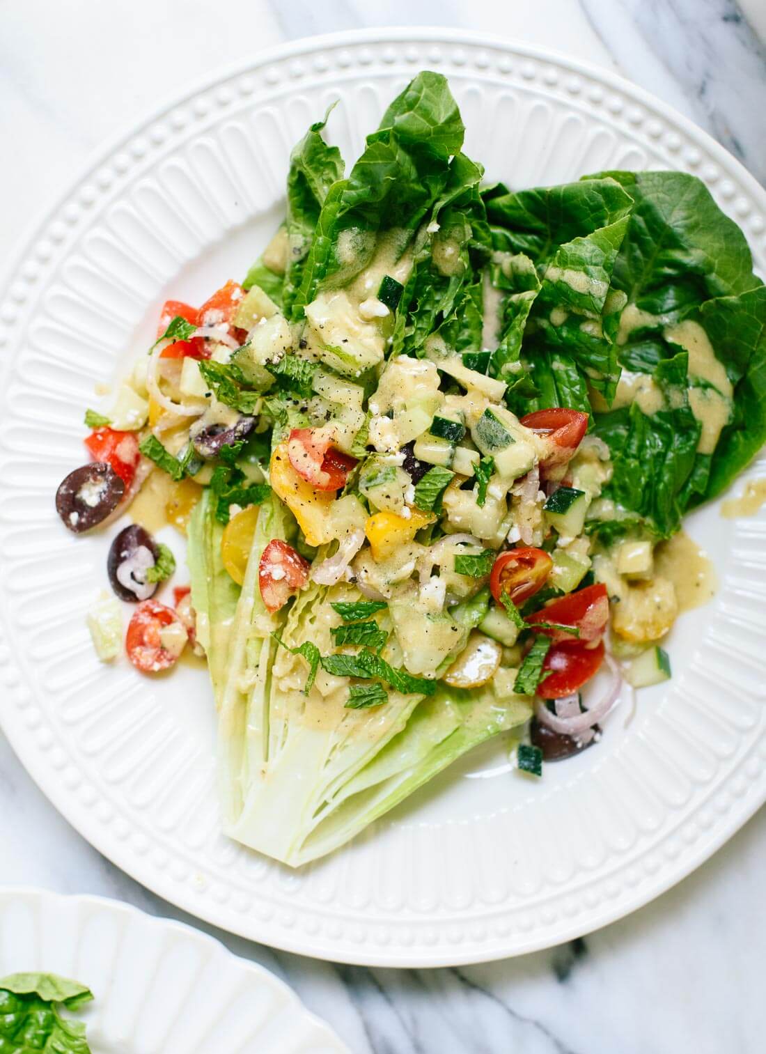 Beautiful Greek salad made with wedges of romaine lettuce, fresh tomatoes, olives and herbs piled on top, and a lemon tahini dressing. Easily vegan. cookieandkate.com